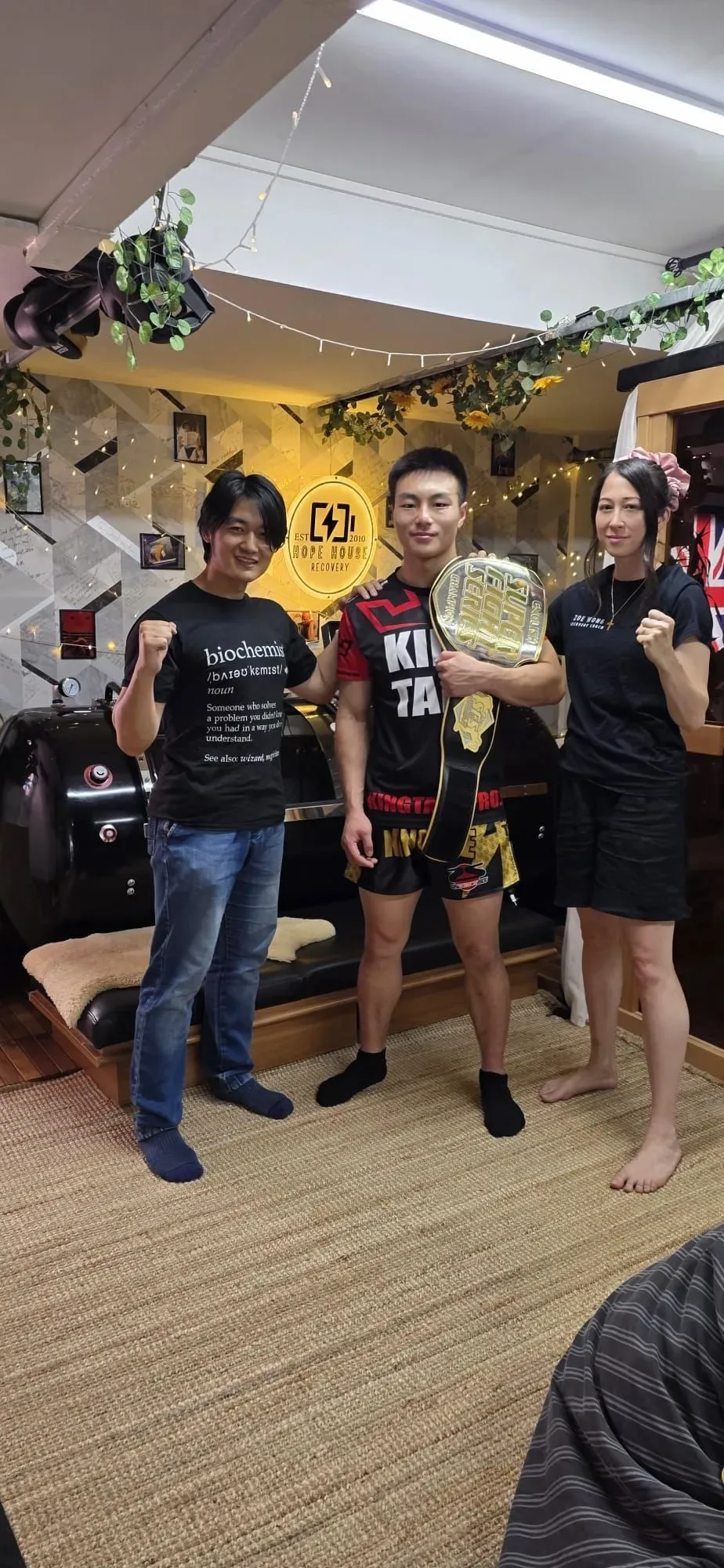 Zoe and Wing stand with Darren, an active kickboxing client, inside Hope House