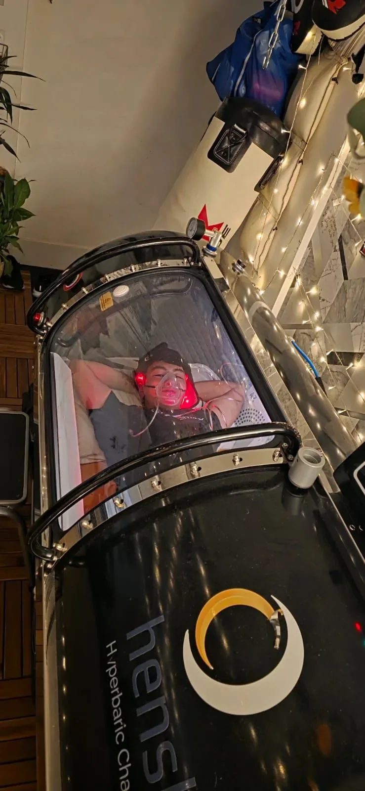 Client rests inside a clear hyperbaric chamber with red light during a session
